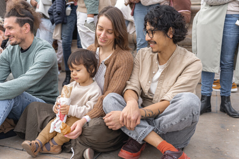 Petit garçon qui mange un sandwich dans les bras de sa maman, papa qui le regarde en souriant à côté lors de #jaifaimjemange 2024 à Bordeaux