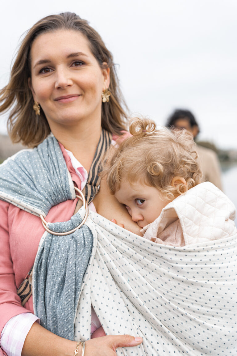 Maman qui marche en allaitant sa fille dans une écharpe de portage de #jaifaimjemange 2024 à bordeaux