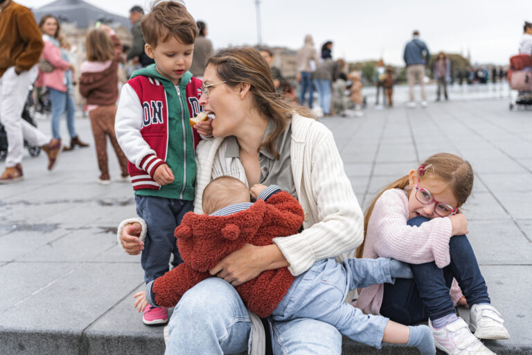 Garçon qui nourrit sa maman qui allaite, la petite soeur boude à côté, au miroir d'eau de Bordeaux pendant #jaifaimjemange 2024