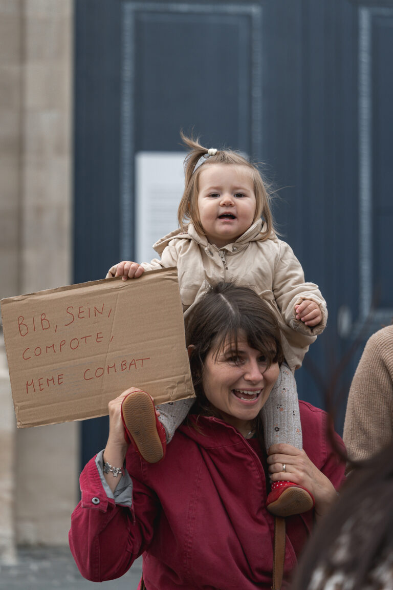 Petite fille sur les épaules de sa mère qui tient une pancarte lors de #jaifaimjemange 2025 par photographe bordeaux