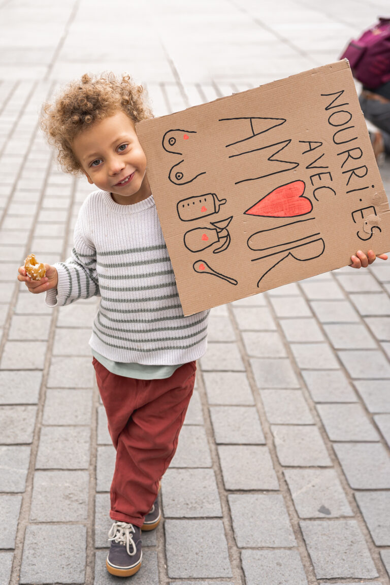 Petit garçon qui tient une pancarte en souriant et en mangeant lors de #jaifaimjemange 2025 devant la mairie à Bordeaux