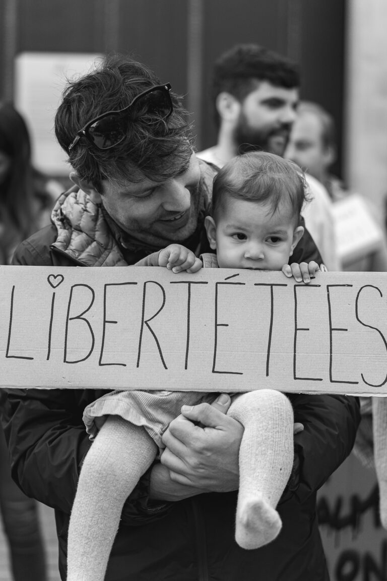 Photo en noir et blanc d'un bébé qui tient une pancarte avec son papa en la mordillant pendant #jaifaimjemange2025 à Bordeaux