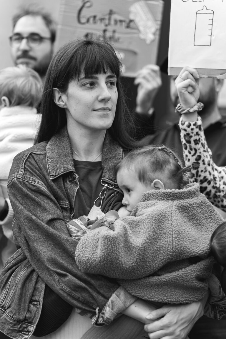 Photo en noir et blanc d'une Maman qui regarde au loin pendant qu'elle allaite sa fille qui regarde du côté opposé pendant #jaifaimjemange 2025 à Bordeaux