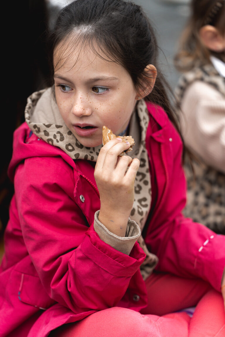 Jeune fille qui mange un cookie en regardant sur le côté dans un manteau rose lors de #jaifaimjemange 2025 à Bordeaux