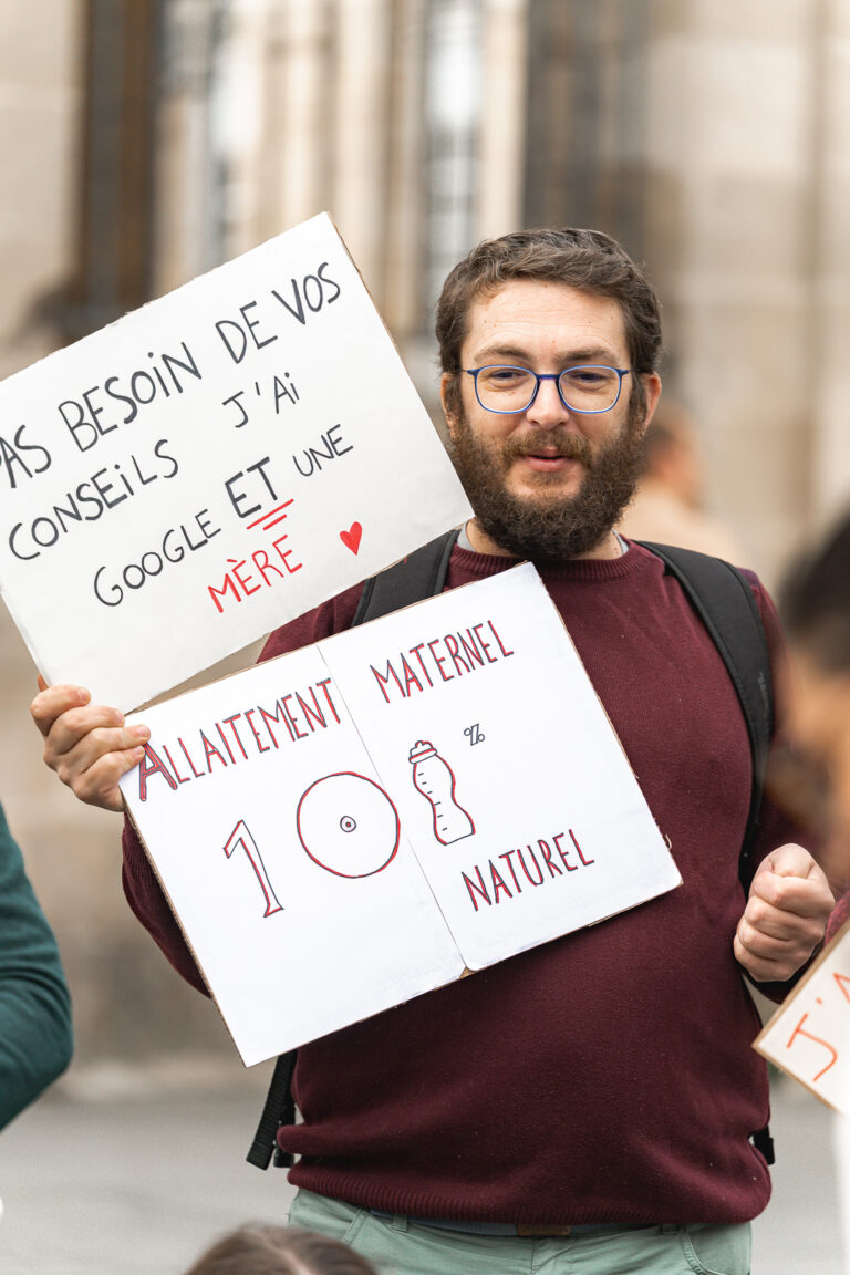 Papa qui tient deux pancartes pour soutenir l'allaitement maternel lors de #jaifaimjemange 2025 à bordeaux, place pey berland