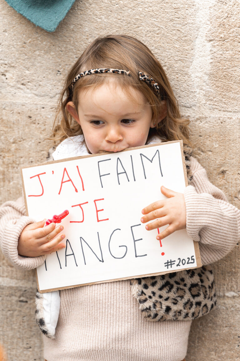 Petite fille qui mord une pancarte avec un bonbon dans la main lors de #jaifaimjemange 2025 à Bordeaux