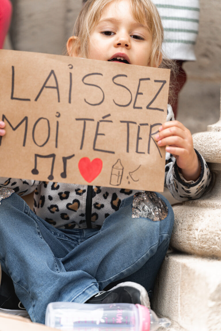 Petite fille qui regarde l'objectif en tenant une pancarte pour l'allaitement maternel lors de #Jaifaimjemange 2025 à Bordeaux, place Pey berland