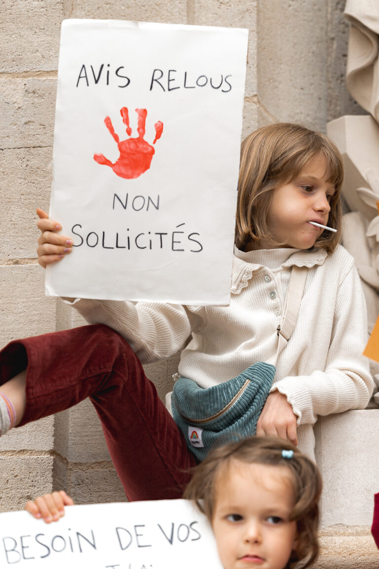 Jeune fille qui tient une pancarte en suçant une sucette en regardant sur la droite lors de #jaifaimjemange 2025 à Bordeaux, place pey berland