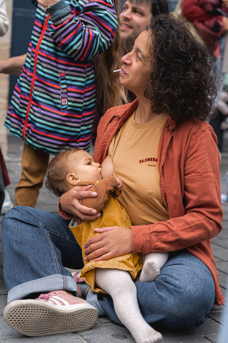 Maman qui allaite son bébé assise par terre en regardant les autres lors de #jaifaimjemange 2025 à Bordeaux