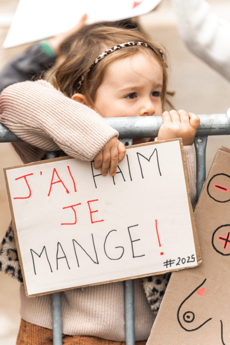 Petite fille qui grimpe sur une barrière en tenant une pancarte lors de #jaifaimjemange 2025 à Bordeaux