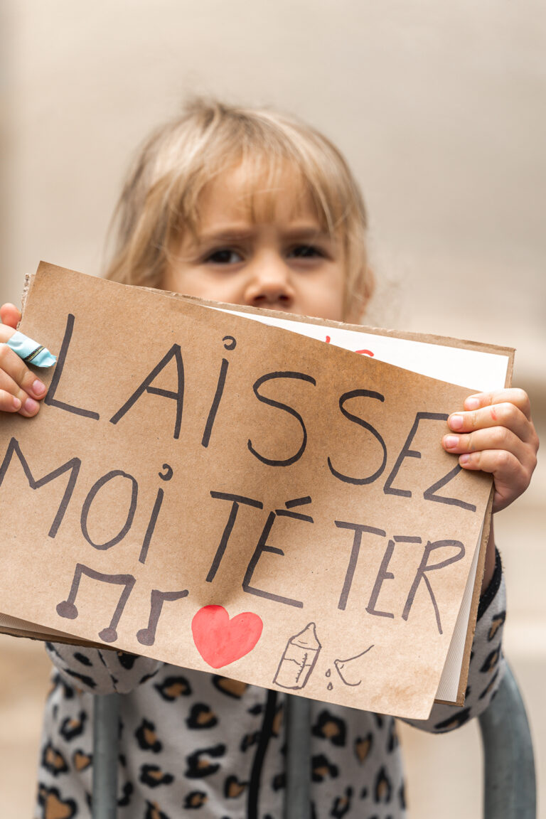 Petite fille qui tient une pancarte pour l'allaitement maternel par dessus une barrière lors de #jaifaimjemange 2025 à Bordeaux