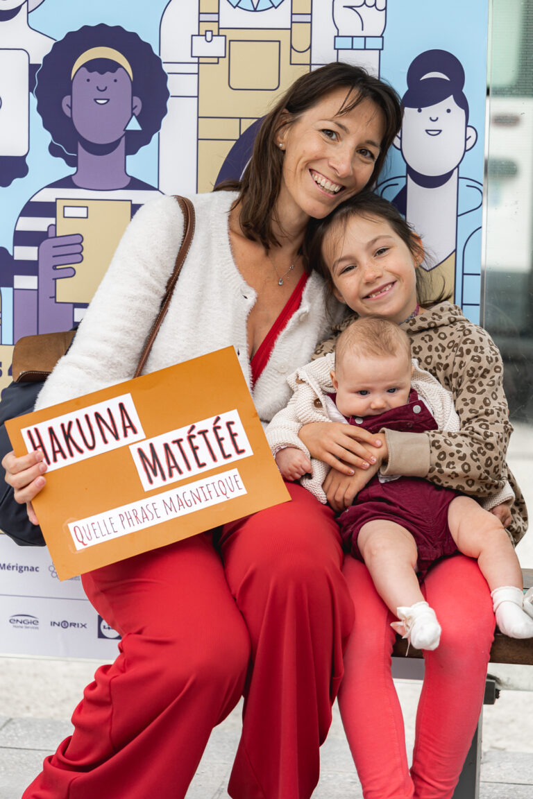 Famille qui pose à un arrêt de tram en souriant avec une pancarte pour l'allaitement maternel lors de #jaifaimjemange 2025 à Bordeaux