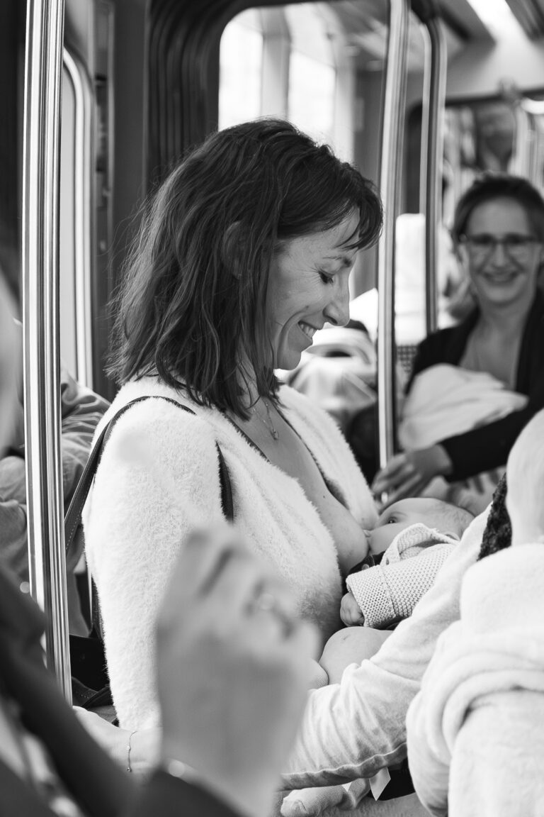 Photo en noir et blanc d'une maman qui allaite son bébé dans le tram en souriant lors de #jaifaimjemange 2025 à Bordeaux