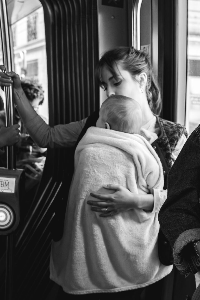 Photo en noir et blanc d'une maman qui tient son bébé en portage debout dans le tram lors de #jaifaimjemange 2025