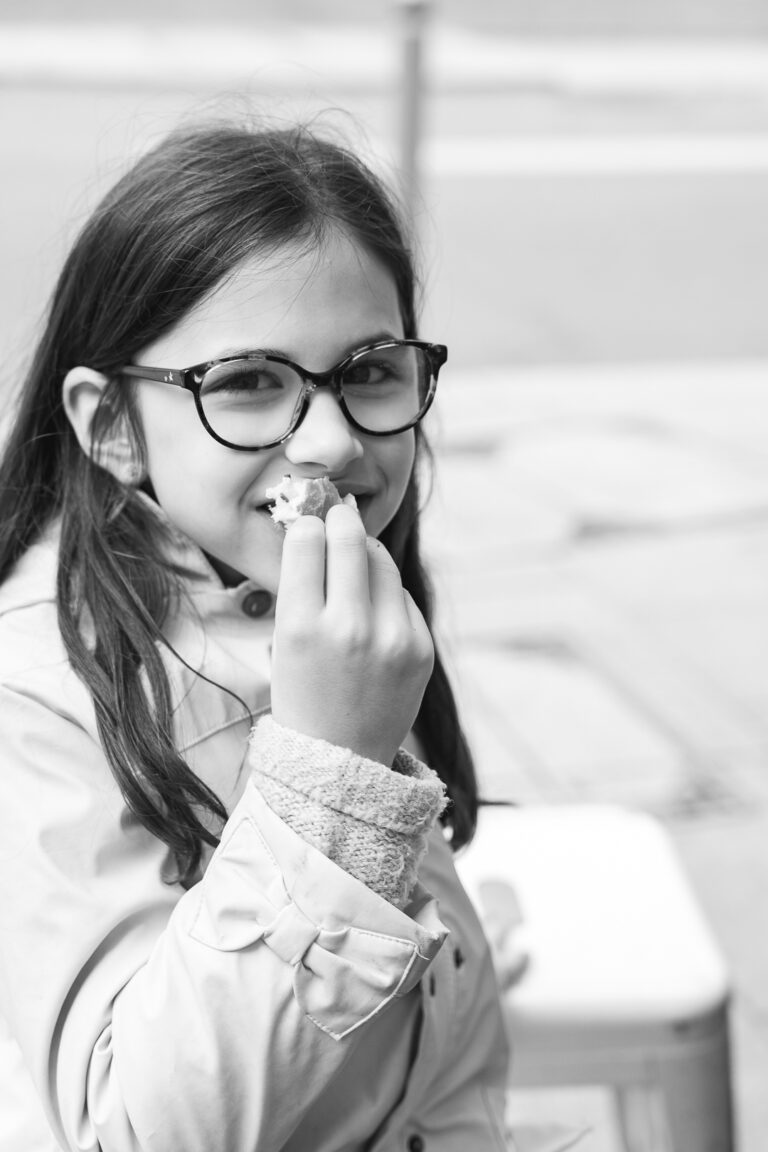 Photo en noir et blanc d'une jeune fille qui mange du pain en souriant lors de #jaifaimjemange 2025 à Bordeaux
