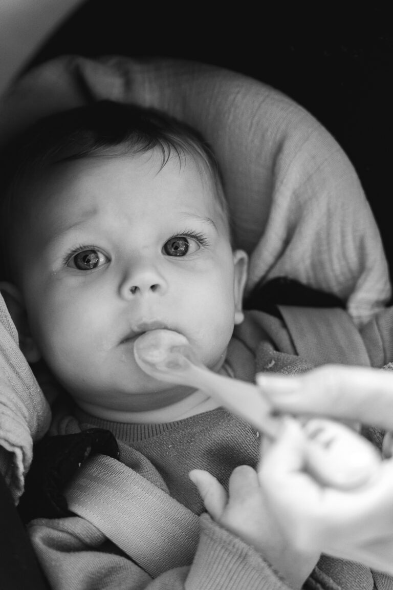 Photo en noir et blanc d'un bébé qui regarde l'objectif en mangeant sa purée lors de #jaifaimjemange 2025 au Carnaval Café à Bordeaux
