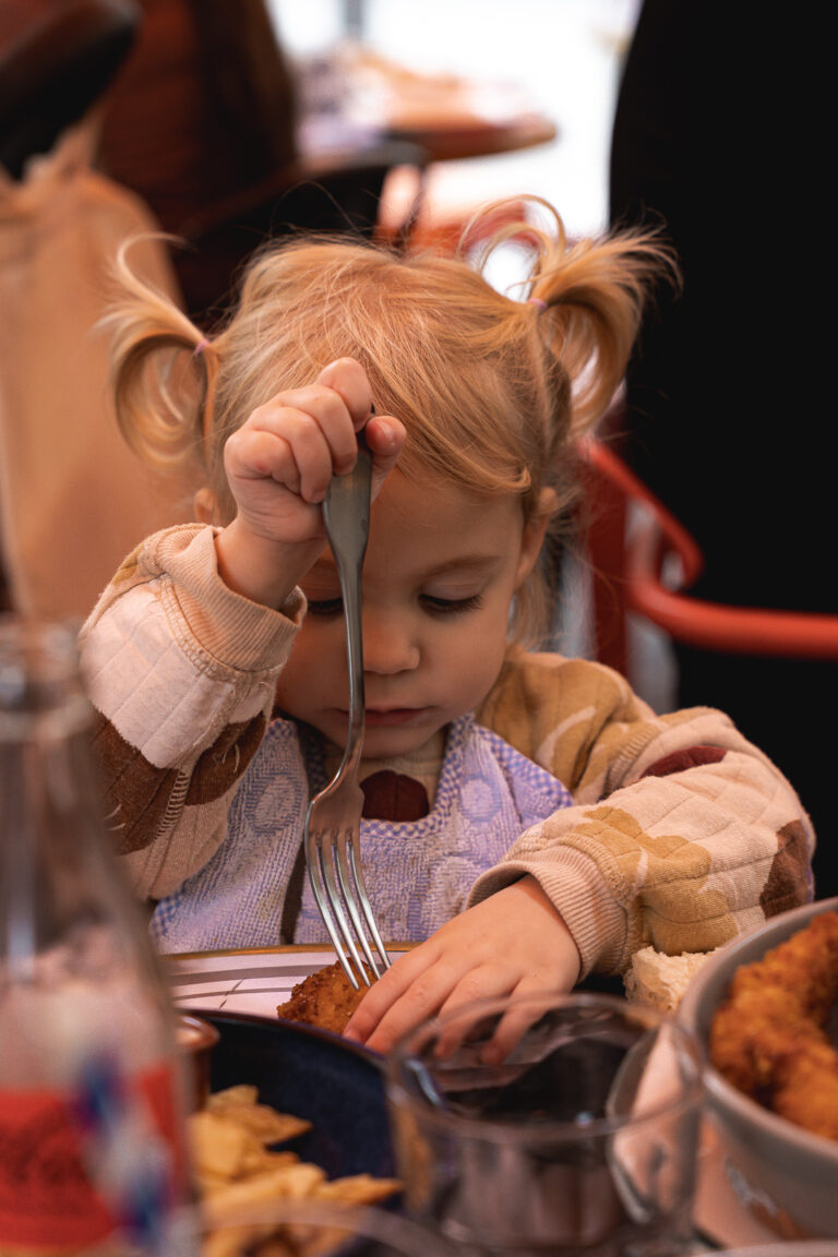 Petite fille concentrée sur le fait de manger avec une fourchette au carnaval café à Bordeaux lors de #jaifaimjemange 2025