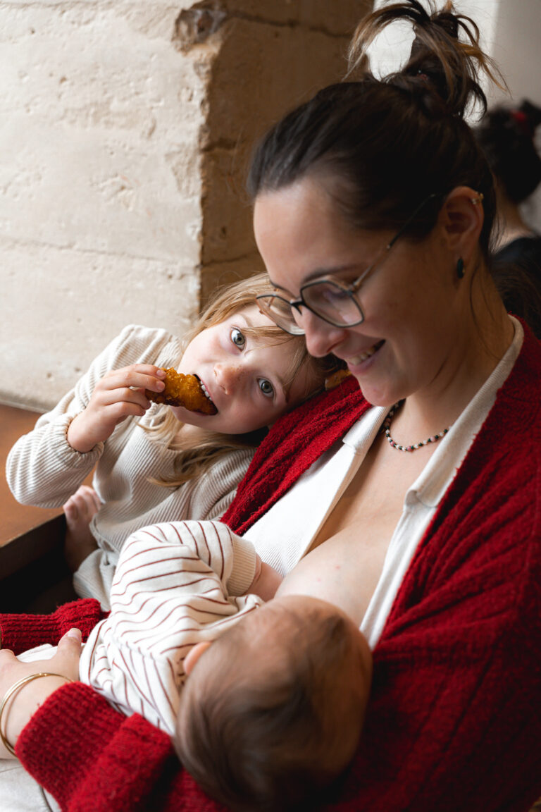 Maman qui allaite son bébé pendant que sa grande fille mange un gâteau en la calinant au carnaval café lors de #jaifaimjemange 2025 à bordeaux