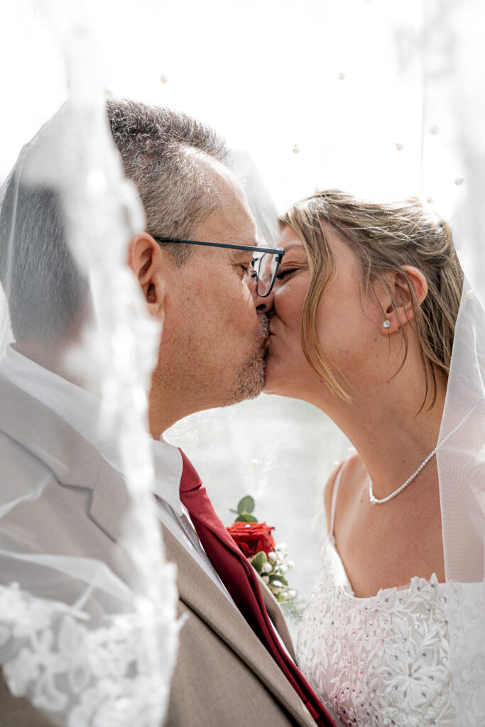 Jeunes mariés s'embrassant sous le voile de la mariée au Parc Majolan de Blanquefort lors de la séance couple de leur mariage