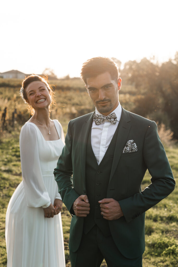 Marié au regard protecteur et mariée se moquant lors de la séance couple de leur mariage dans les vignes au coucher du soleil