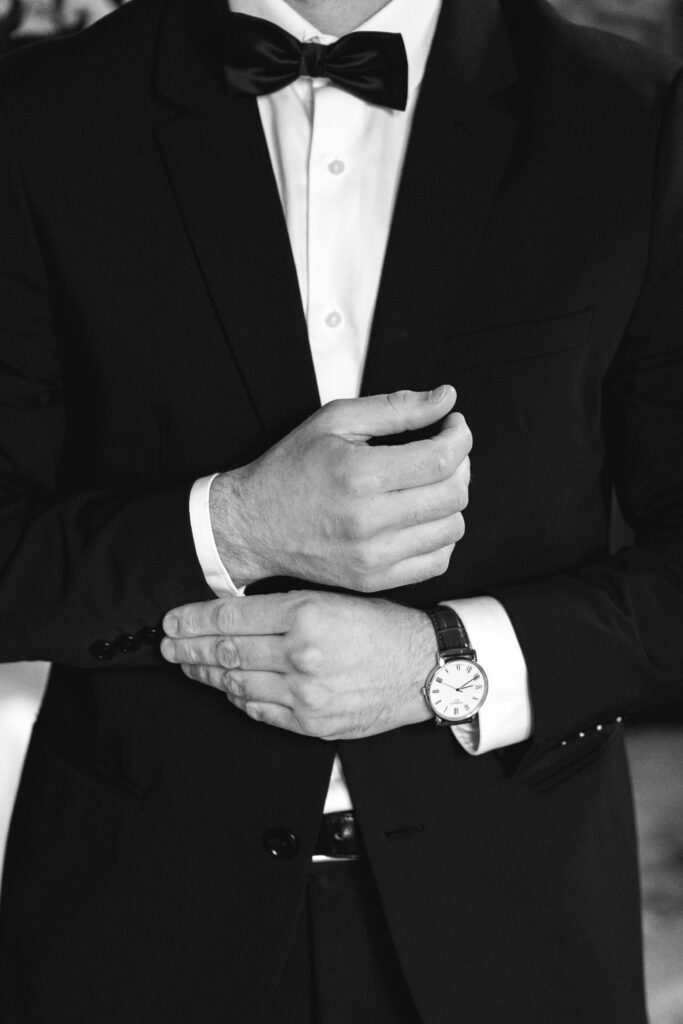 Photo en noire et blanche des détails sur les mains du futur marié qui met ses manchettes lors des préparatifs de son mariage