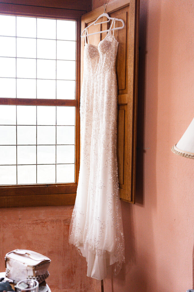 Robe de la mariée suspendue devant la fenêtre de sa chambre lors des préparatifs de son mariage