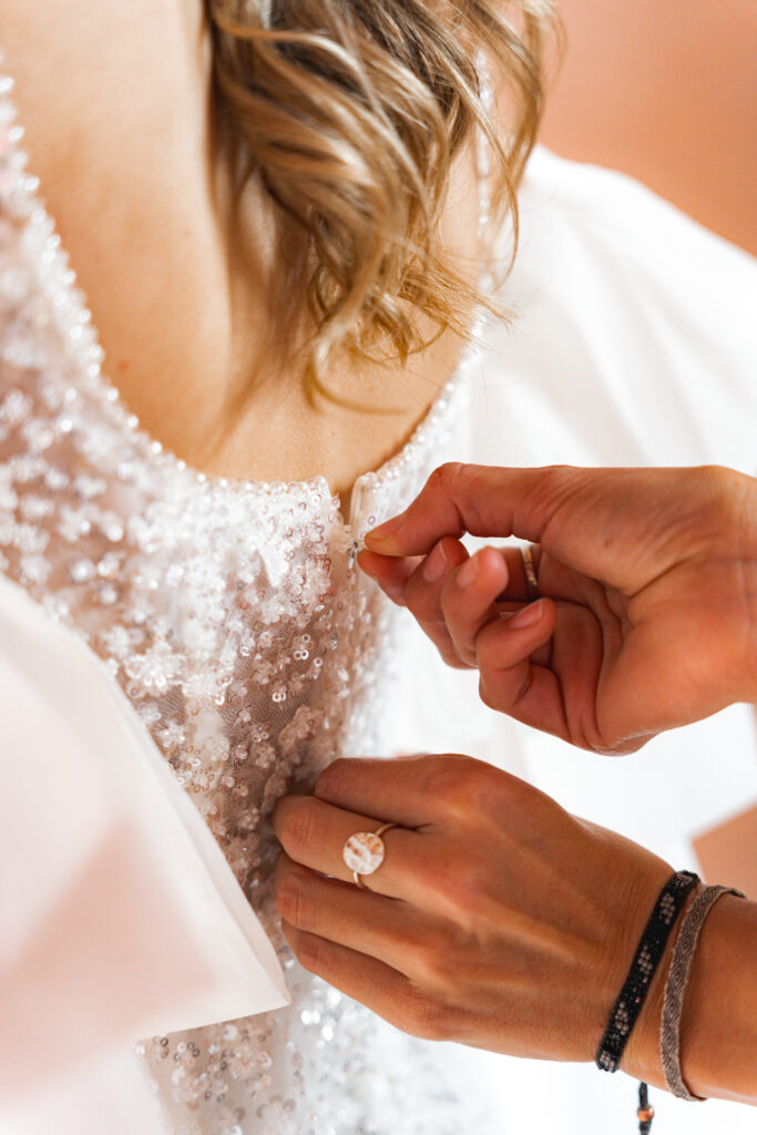 Détails des mains de la soeur de la mariée qui remonte la fermeture éclair de la robe de la mariée lors des préparatifs de mariage