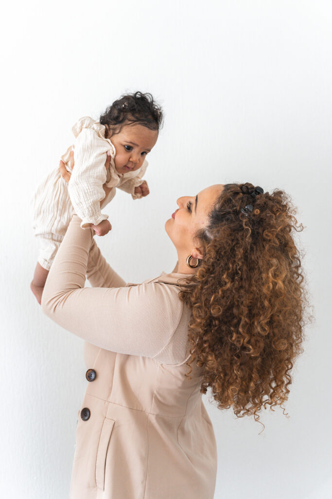 Bébé tenue en l'air par sa maman lors d'une séance naissance lifestyle à domicile à Pessac