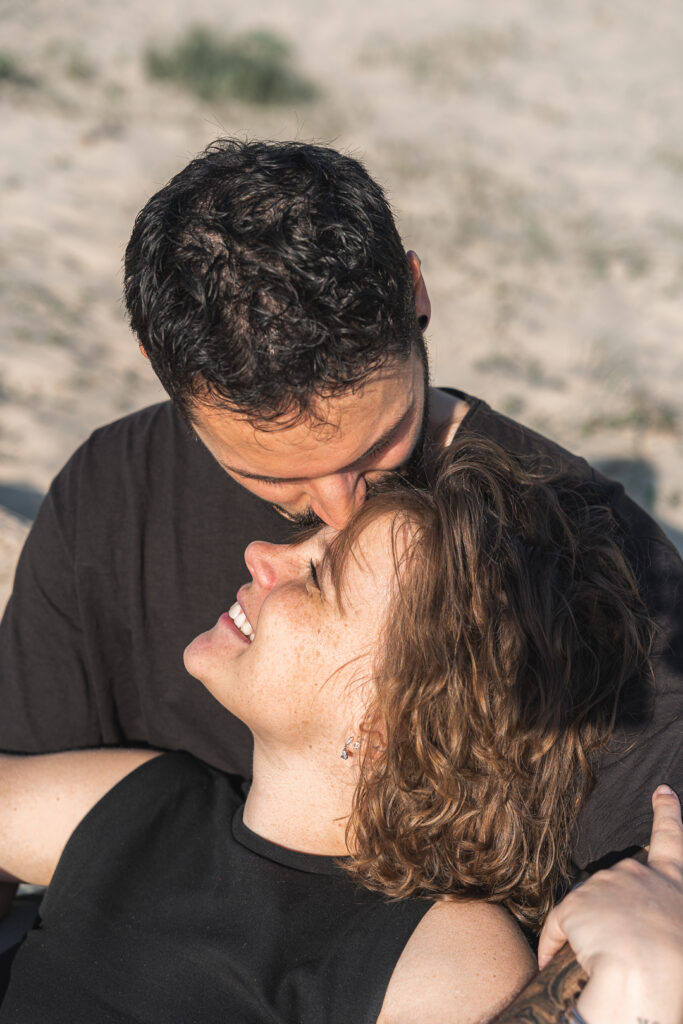 Homme qui embrasse le front de sa femme souriante lors d'une séance couple aux Dunes du Pilat