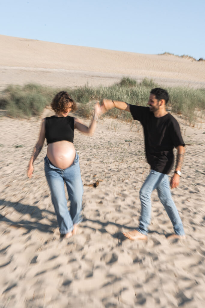 Photo en flou de bouger d'un homme qui danse avec sa femme enceinte lors d'une séance grossesse à la plage des dunes du pilat