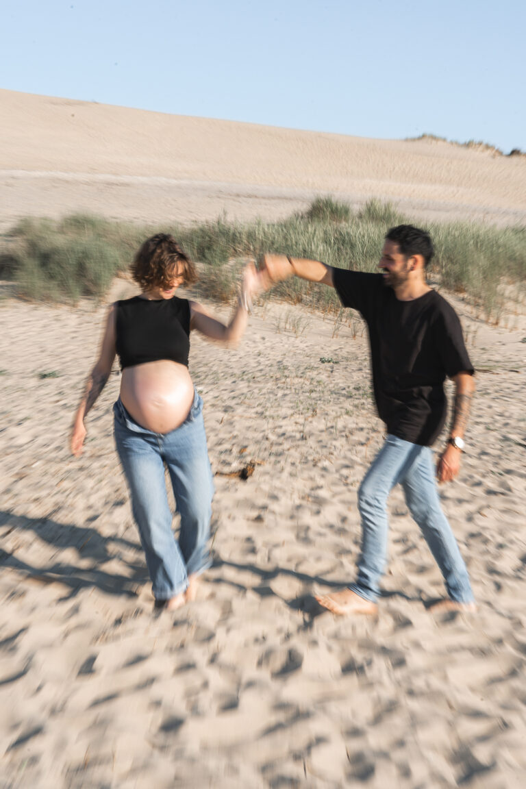 Photo en flou de bouger d'un homme qui danse avec sa femme enceinte lors d'une séance grossesse à la plage des dunes du pilat