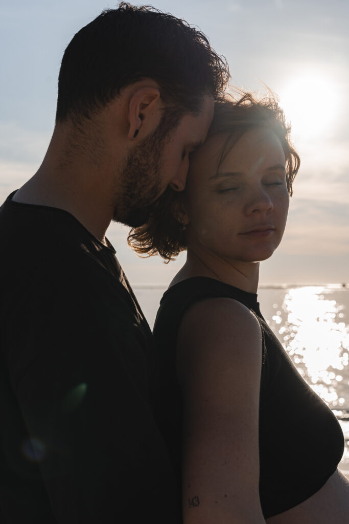 Front d'un homme contre la tempe de sa femme qui a les yeux fermés pendant une séance couple au coucher du soleil aux Dunes du Pilat