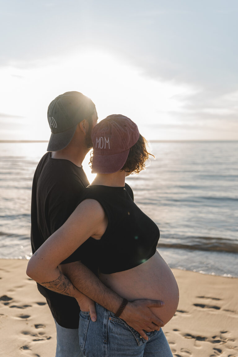 Couple avec leurs casquettes mom et dad lors d'une séance grossesse au coucher du soleil aux dunes du pilat