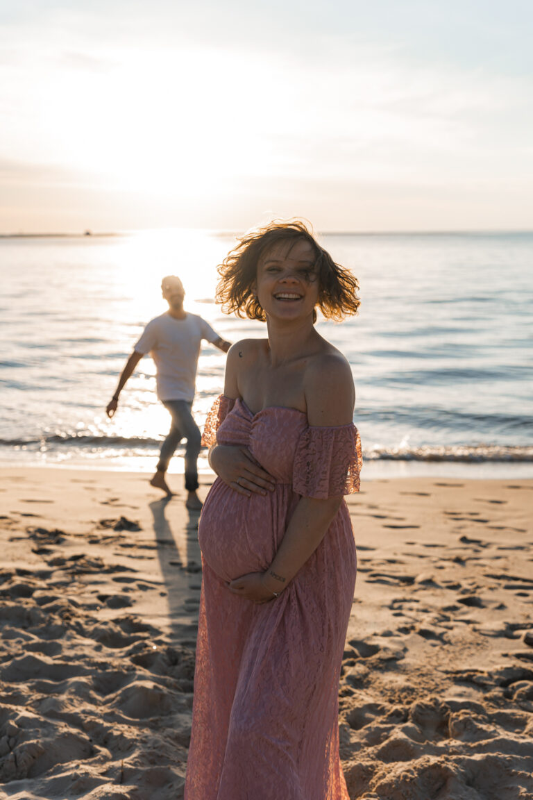 Future maman qui rit face aux bêtises de son époux lors d'une séance photo grossesse au coucher du soleil aux dunes du pilat