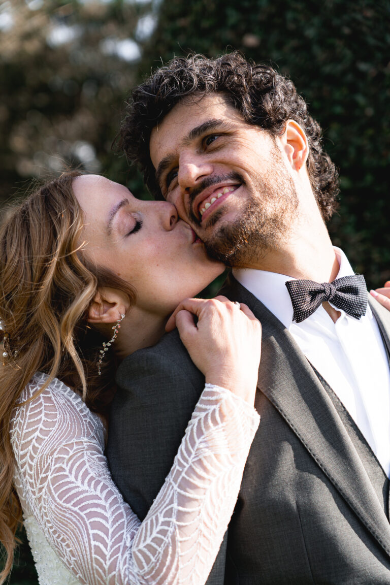 Mariée qui embrasse son mari souriant sur la joue pendant la séance photo de couple de leur mariage civile à Pessac