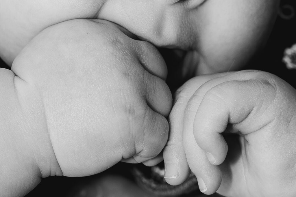 Photo en noir et blanc de détails d'un bébé qui suce ses mains pendant une séance famille lifestyle à domicile à mérignac