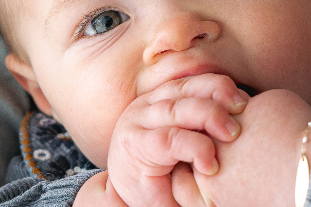 Détails des yeux d'un bébé qui suce ses mains pendant une séance famille lifestyle à domicile à mérignac