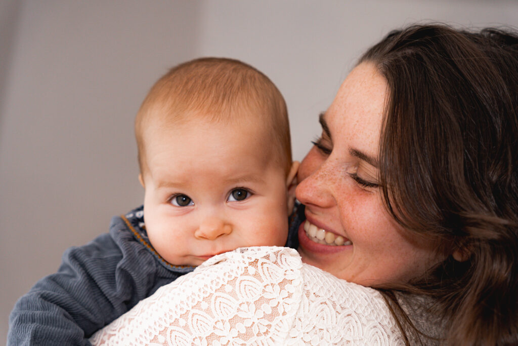 Maman qui tient son bébé dans les bras et lui fait un grand sourire pendant une séance famille lifestyle à domcile à Mérignac