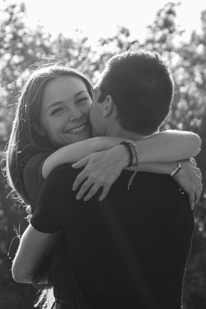 Photo en noir et blanc d'un couple enlacé dont la femme sourit lors d'une séance couple au parc de Majolan à Blanquefort