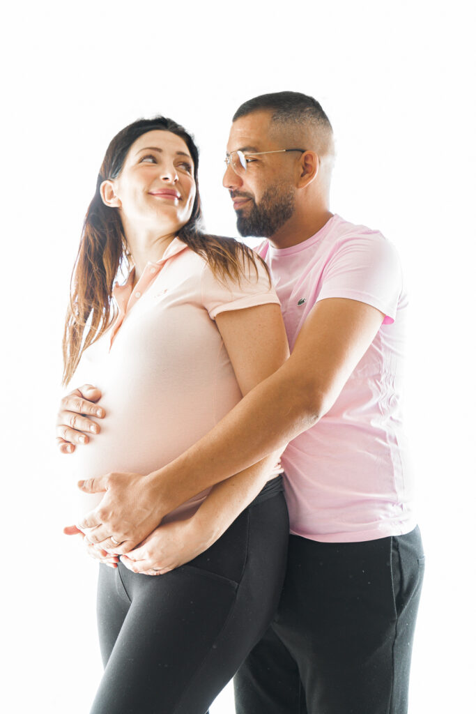Femme enceinte qui regarde son mari dans les yeux en touchant son ventre lors d'une séance grossesse au home Studio à bordeaux