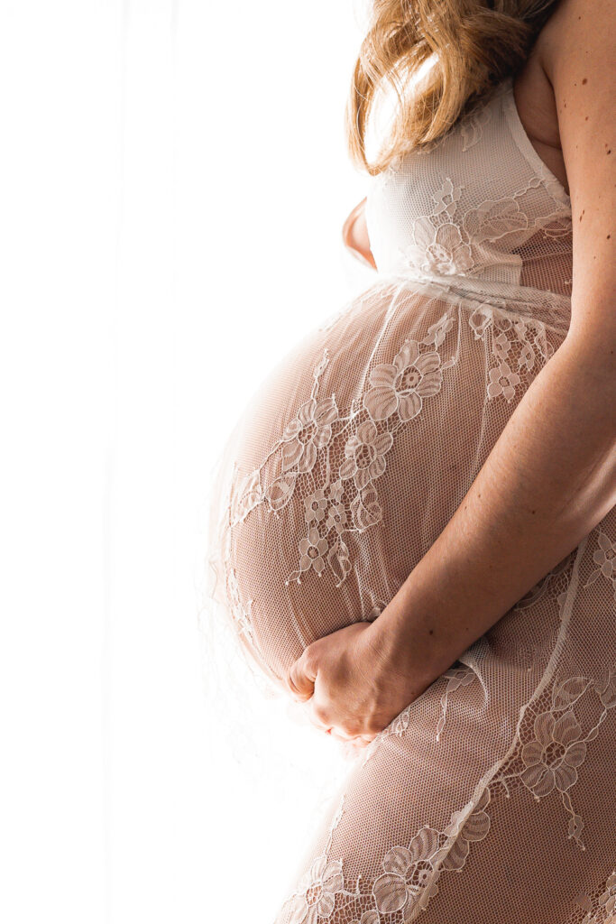 Gros plan du ventre d'une femme enceinte dans une robe en dentelle lors d'une séance grossesse au home studio à Bordeaux
