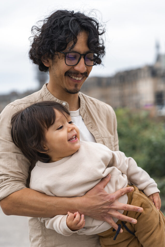 Papa qui tient son enfant dans les bras et le regarde en souriant lors d'une séance famille lifestyle en extérieur sur les quais de bordeaux