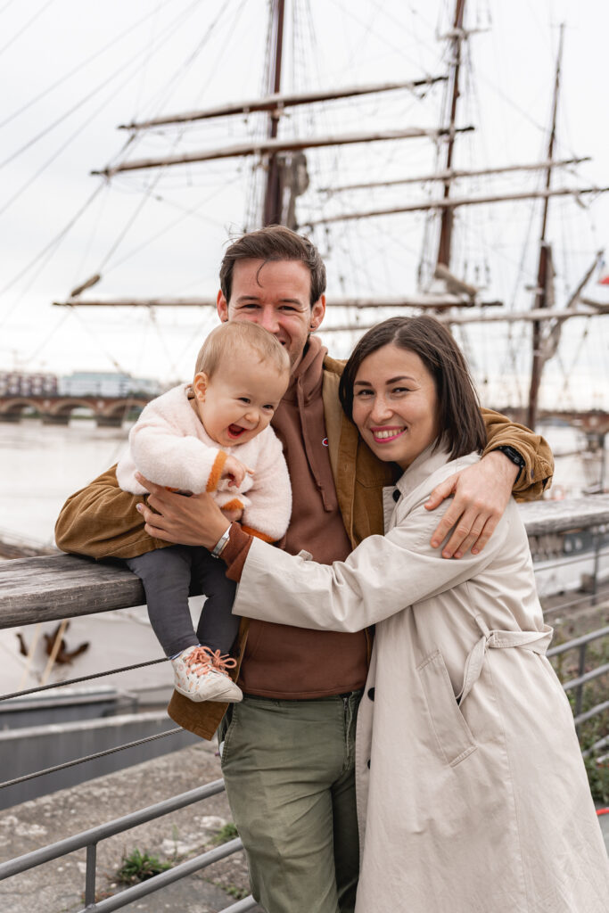 Parents qui tiennent leur bébé mort de rire lors d'une séance famille lifestyle en extérieur sur les quais de bordeaux