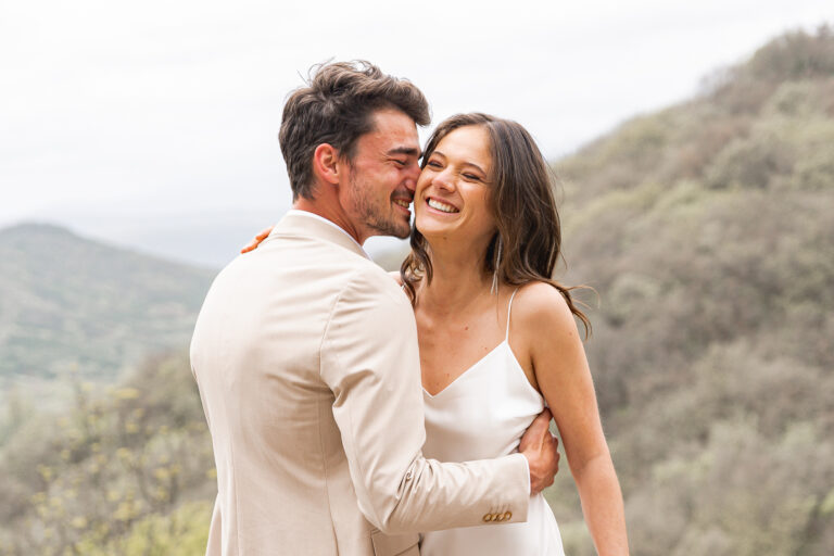 Marié qui fait rire sa femme en lui parlant à l'oreille lors de la séance photo couple de leur reportage mariage à la montagne