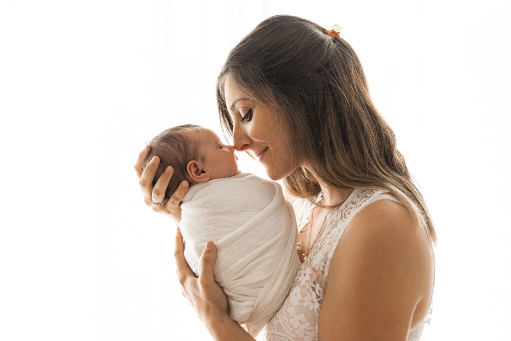Bébé nouveau-né emmailloté nez à nez avec sa maman au sourire doux lors d'une séance naissance à mon home studio à Bordeaux
