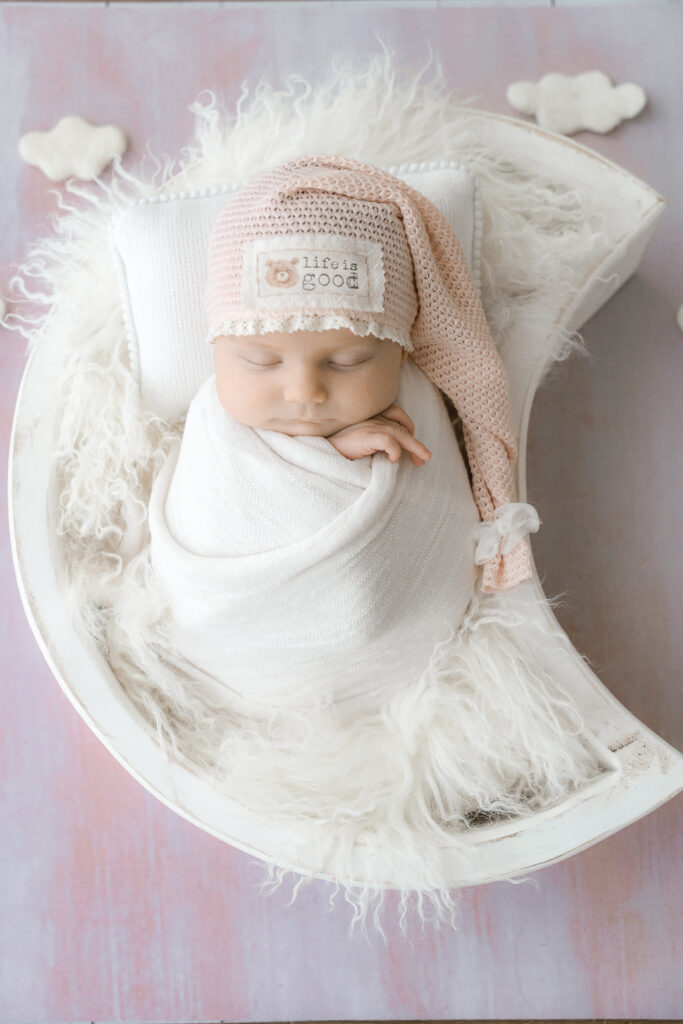 Bébé nouveau-né emmailloté en baby-posing dans une lune avec fond et bonnet rose lors d'une séance naissance au home studio de Bordeaux