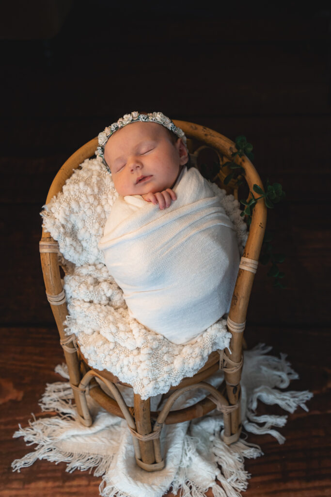 Bébé nouveau-né emmailloté en baby posing dans une chaise en bois lors d'une séance naissance à mon home studio de Bordeaux