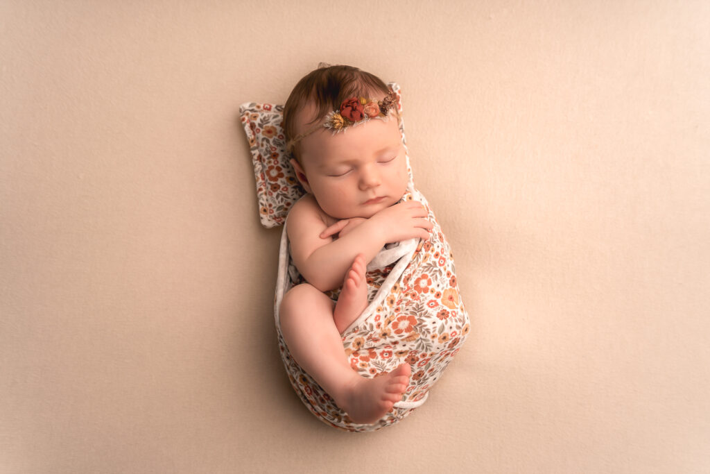 Bébé nouveau-né semi-emmaillotté dans un tissu à fleur lors d'une séance naissance à mon home studio de Bordeaux