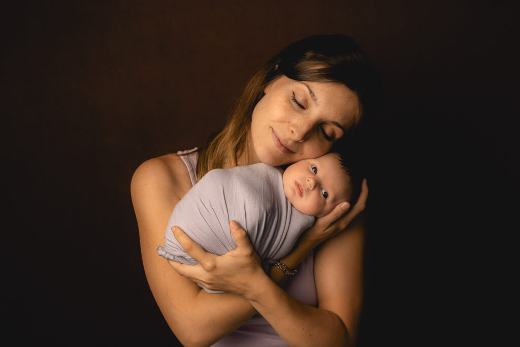 Bébé nouveau-né emmaillotée en baby-posing dans les bras de sa maman lors d'une séance naissance à mon home studio à Bordeaux