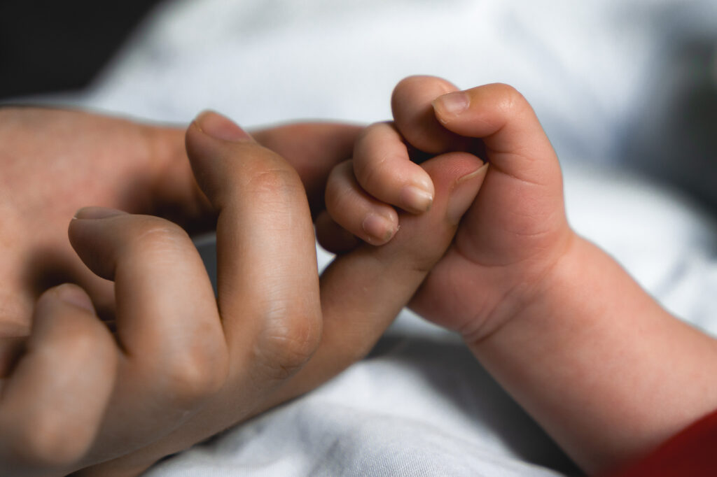 Détails d'un bébé nouveau-né qui tient le doigt de sa maman lors d'une séance naissance lifestyle à domicile à Blanquefort